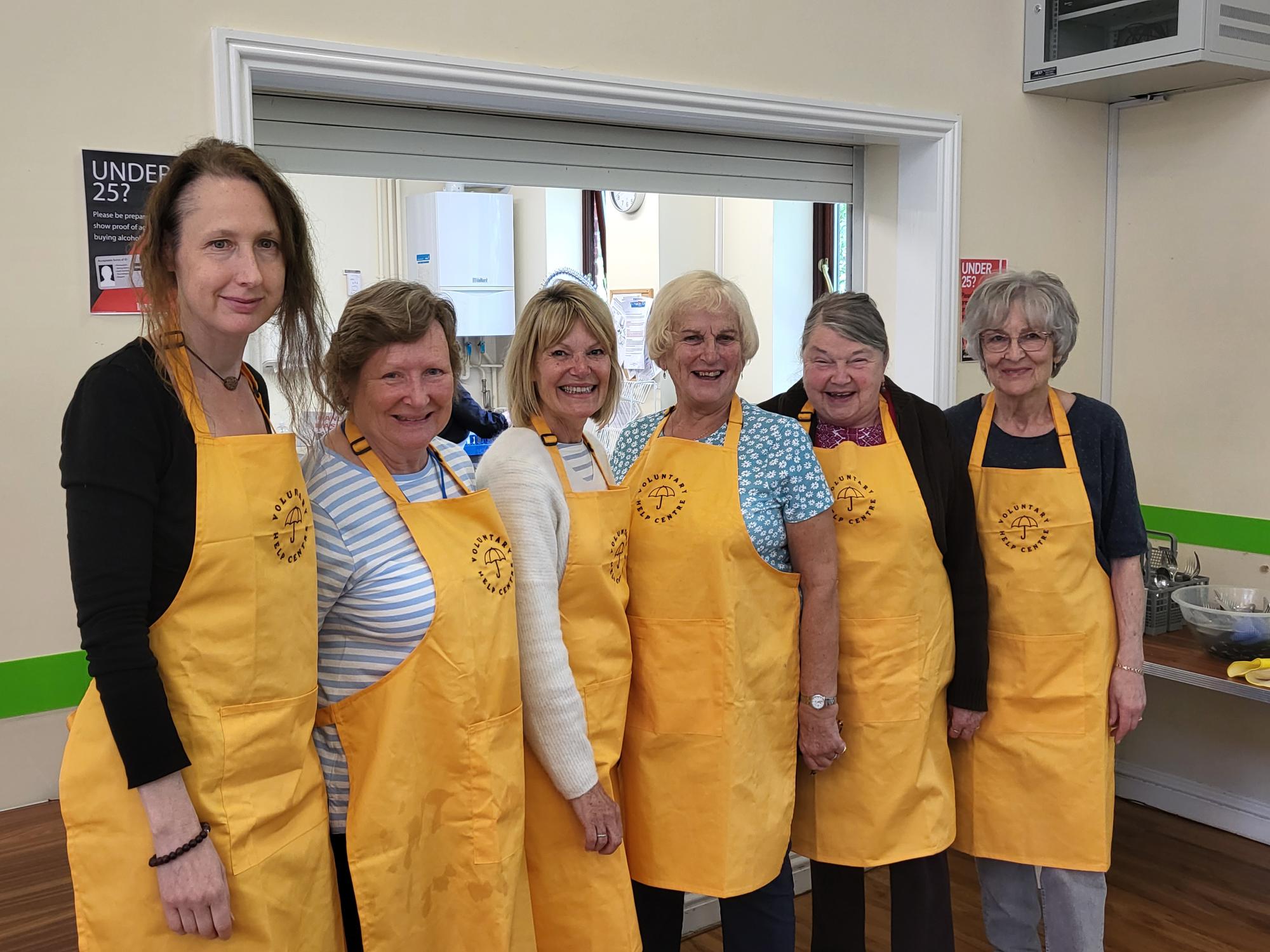 6 lunch club volunteers showing off their new yellow aprons